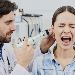 Patient in distress during ear syringing as a doctor uses a large syringe at the ear.